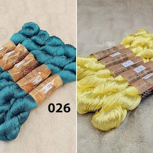 以下が含まれることがあります： 2つの刺繍糸の糸巻き、1つはティールブルー、もう1つはイエロー。糸巻きは茶色の紙で包まれており、ティールブルーの糸巻きには「14 720」と「026」、イエローの糸巻きには「105」という白い文字が書かれています。