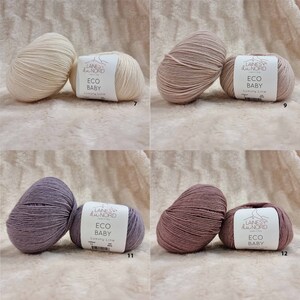 May include: Four skeins of yarn in different colors: white, light pink, purple, and pink. Each skein has a label that reads "Laines du Nord Eco Baby Luxury Line".