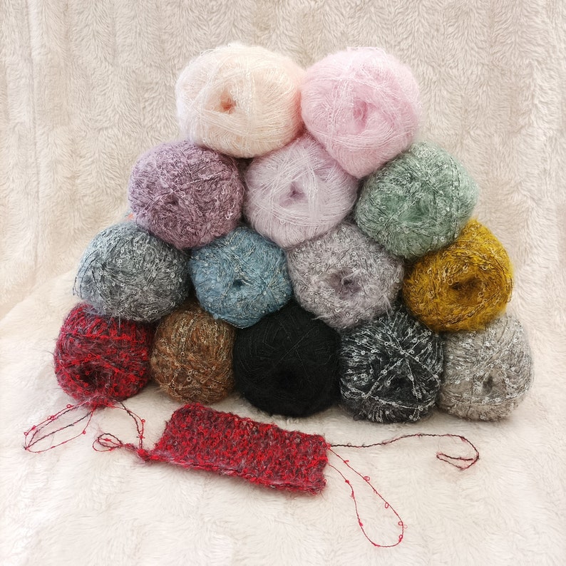 Puede incluir: Una colecci&oacute;n de 14 ovillos de lana en varios colores, incluyendo rosa, morado, verde, marr&oacute;n y gris. La lana est&aacute; dispuesta en forma de pir&aacute;mide sobre una superficie blanca y peluda.