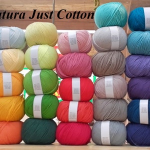 May include: A collection of DMC Natura Just Cotton yarn skeins in various colours, stacked in rows. The colours include light blue, yellow, pink, green, orange, red, grey, purple, brown, and black.