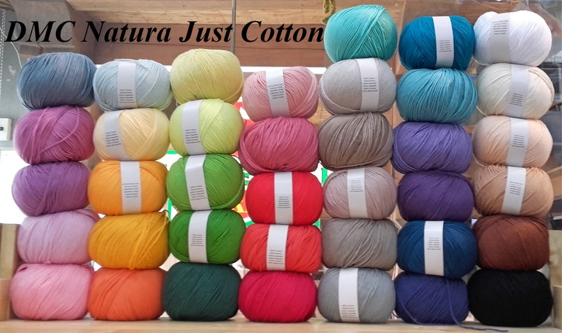 May include: A collection of DMC Natura Just Cotton yarn skeins in various colours, stacked in rows. The colours include light blue, yellow, pink, green, orange, red, grey, purple, brown, and black.
