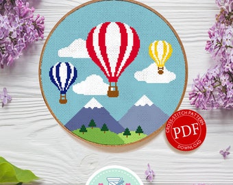 May include: Cross stitch pattern PDF download for a colorful hot air balloon design. The pattern features three hot air balloons in red, yellow, and blue, flying over a mountain range with green trees and white clouds against a blue sky.