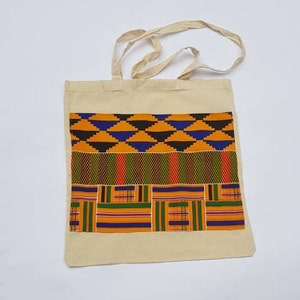 May include: A beige tote bag with a colorful African print design. The print features geometric shapes in shades of orange, yellow, blue, green, and black.