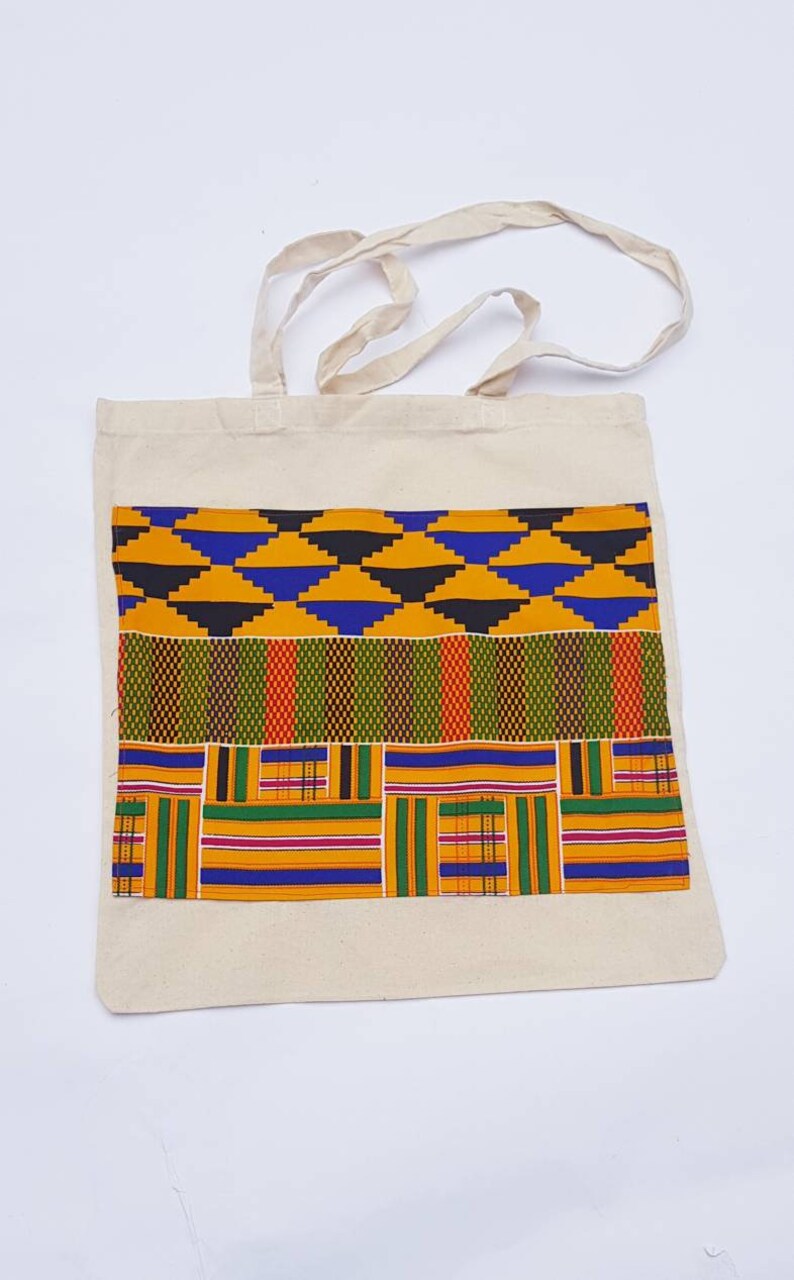 May include: A white canvas tote bag with a colorful African print design. The print features a combination of yellow, blue, green, red, and black geometric patterns.