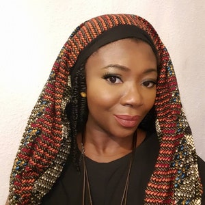 Pu&ograve; includere: Una donna indossa una camicia nera e un turbante con motivi colorati. Il turbante ha una fascia nera intorno alla fronte ed &egrave; legato dietro il collo. La donna indossa una collana.