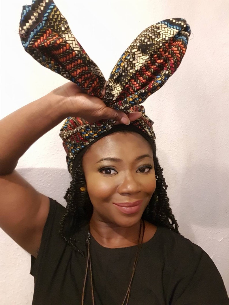 Pu&ograve; includere: Una donna indossa una camicia nera con un turbante a motivi con due estremit&agrave; lunghe e appuntite. Il turbante &egrave; legato in un nodo sulla cima della sua testa e le estremit&agrave; sono drappeggiate sulle sue spalle.