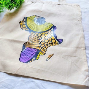 May include: A white canvas tote bag with a colorful graphic of the continent of Africa. The graphic is made up of yellow, orange, purple, and black geometric shapes.