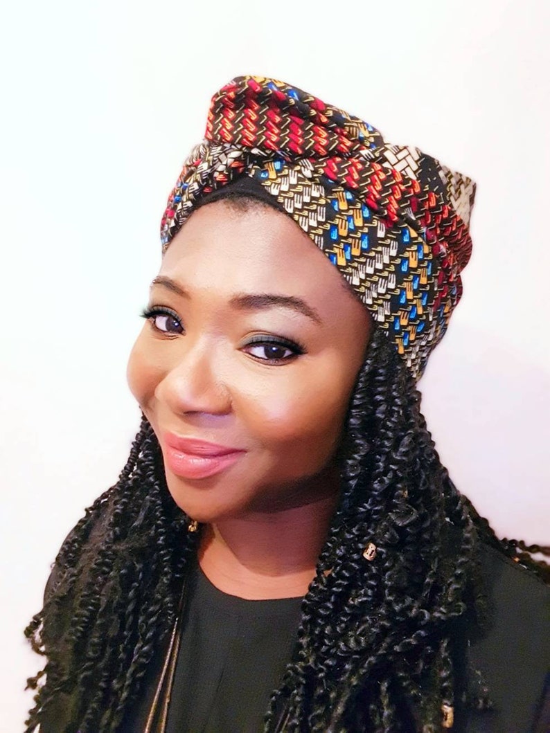 Pu&ograve; includere: Una donna con i capelli scuri e ricci indossa un turbante con motivi colorati. Il turbante &egrave; fatto di tessuto con un motivo geometrico in tonalit&agrave; di rosso, blu, giallo e nero.