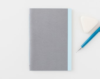 May include: A gray notebook with a light blue stripe down the spine. A blue pencil and a white eraser are on a white surface next to the notebook.