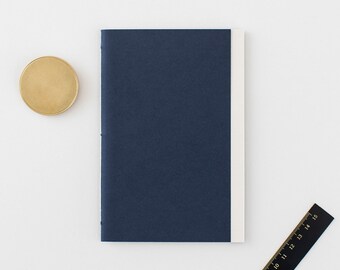 May include: A dark blue notebook with a white spine. The notebook is closed and lying flat on a white surface.