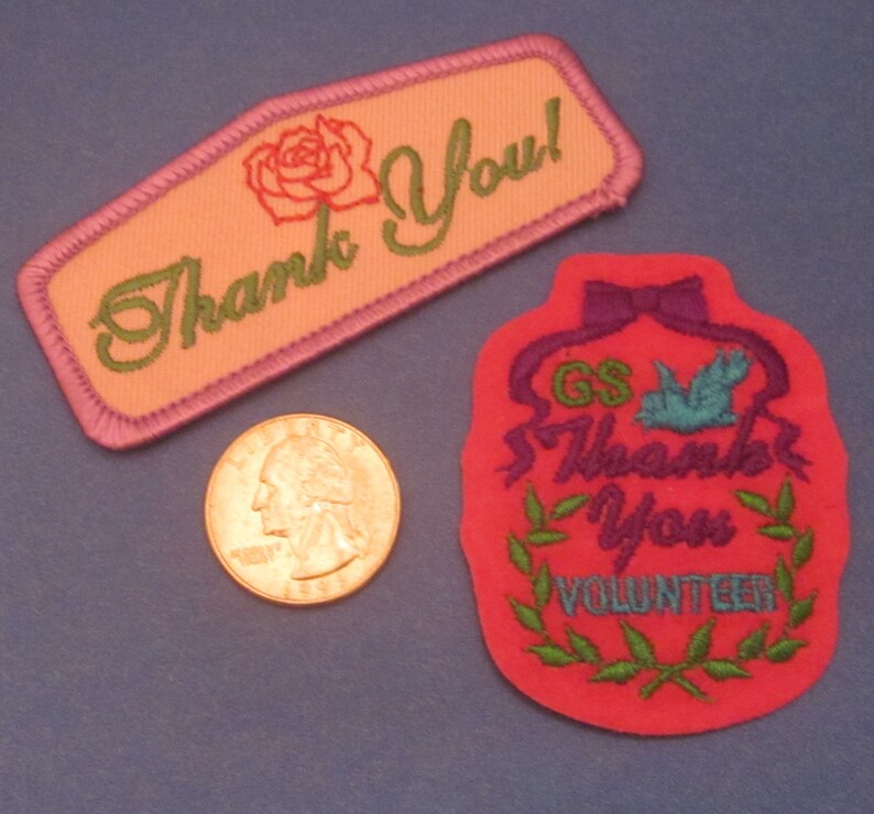 May include: Two embroidered patches with "Thank You" text. One is peach with a rose and green text, the other is red with a dove, bow, and "Thank You Volunteer" text. A quarter is next to the patches.