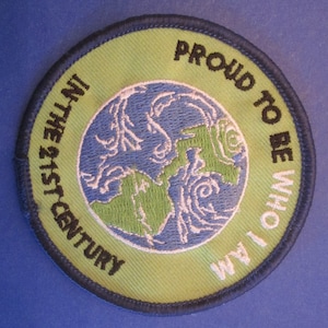 May include: A green and blue embroidered patch with the text "Proud to be who I am in the 21st century" around a stylized image of the Earth.