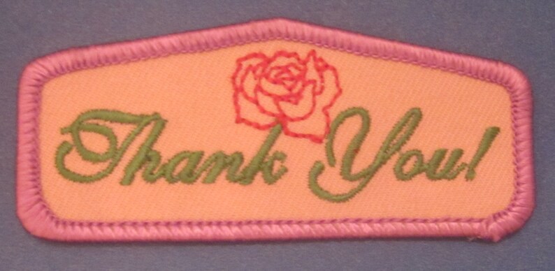May include: Embroidered patch with a peach-colored background and a pink border. The patch features the words "Thank You!" in green script, and a red rose illustration.