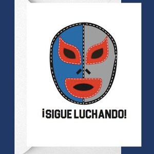 May include: Greeting card with a luchador mask design. The mask is split into blue and grey sections with red eye and mouth details. The text "¡SIGUE LUCHANDO!" is printed below the mask in black.