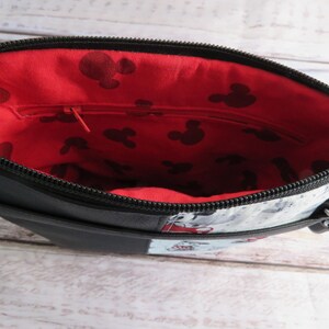 Puede incluir: Bolso bandolera negro con forro rojo y blanco con estampado de Mickey Mouse. El bolso tiene cierre de cremallera y una correa.