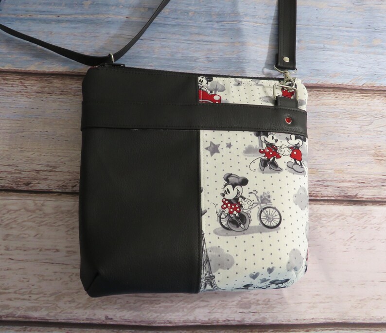 Puede incluir: Bolso bandolera de Mickey Mouse y Minnie Mouse en blanco y negro con una solapa de piel sint&eacute;tica negra. El bolso tiene un fondo blanco con lunares negros y estrellas.