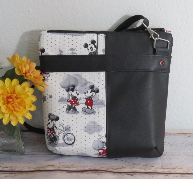 Puede incluir: Bolso de tela con estampado de Mickey Mouse y Minnie Mouse en blanco y negro con solapa y correa de piel sint&eacute;tica negra. El bolso tiene cierre de cremallera y un peque&ntilde;o bolsillo en la parte delantera.