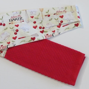 May include: A red and white kitchen towel with a pattern of cherries, hearts, and the text "Bless the Baker" and "Kiss the Cook".