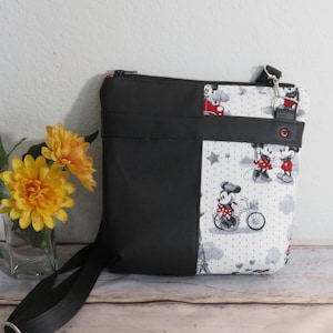 Puede incluir: Bolso bandolera de Mickey Mouse y Minnie Mouse en blanco y negro con cremallera y correa negras. El bolso tiene un panel de tela negra en la parte delantera.