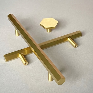 Puede incluir: Tres tiradores de armario de color dorado, incluyendo dos tiradores rectangulares y una perilla hexagonal.