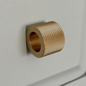 May include: A gold-toned, round cabinet knob with a textured, diamond-shaped pattern.