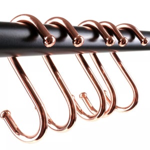 May include: Six rose gold S-shaped hooks hanging on a black metal bar. The hooks are all the same size and shape, and they are evenly spaced apart.