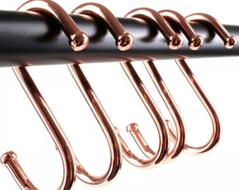 May include: Six rose gold S-shaped hooks hanging on a black metal bar. The hooks are all the same size and shape, and they are evenly spaced apart.