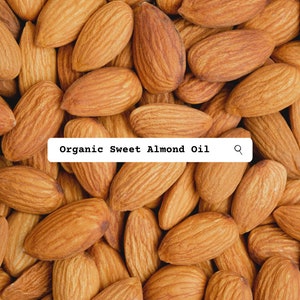K&ouml;nnte beinhalten: Eine dichte Ansammlung ganzer brauner Mandeln mit texturierten, gerillten Schalen. Ein wei&szlig;es rechteckiges Etikett ist &uuml;ber den N&uuml;ssen zentriert und zeigt den schwarzen Text Organic Sweet Almond Oil sowie ein kleines schwarzes Lupensymbol.