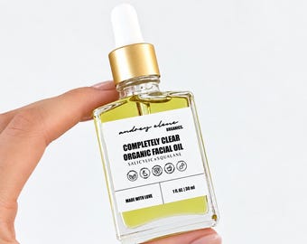 May include: A square glass bottle of yellow facial oil with a gold dropper cap. The white label reads: andrey elene ORGANICS. COMPLETELY CLEAR ORGANIC FACIAL OIL SALICYLICxSQUALANE. Includes icons, MADE WITH LOVE, and 1 fl. oz. | 30 ml.