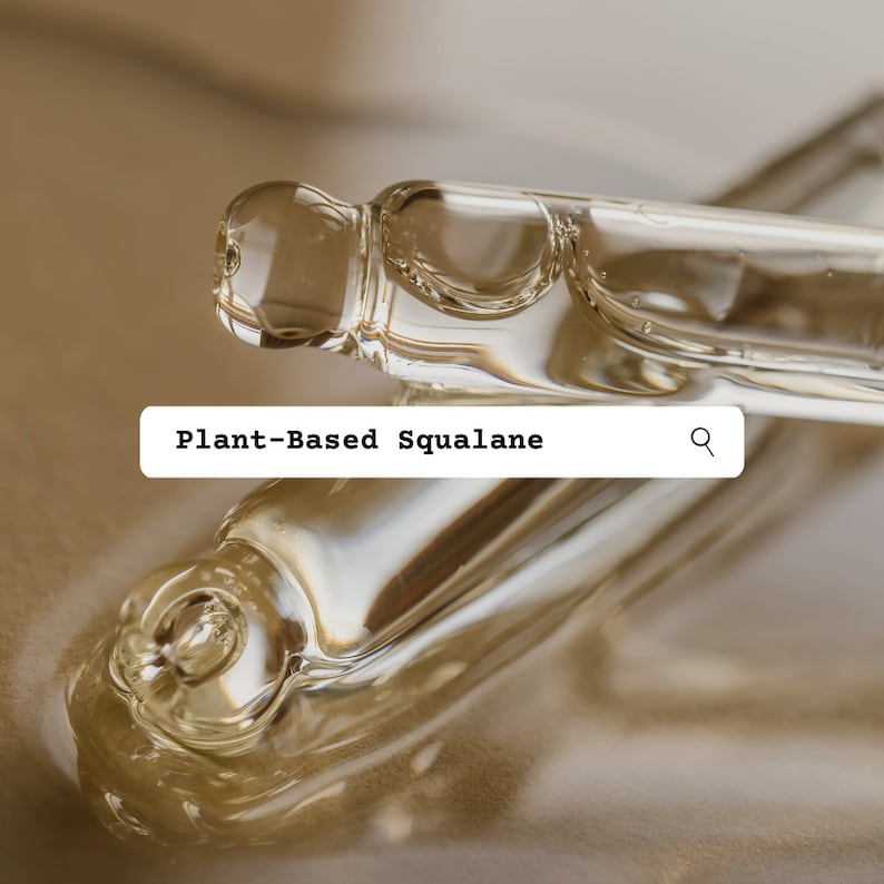 May include: Two clear glass bottles with a dropper tip filled with a light yellow liquid. The bottles are lying on a light brown surface. The text "Plant-Based Squalane" is displayed in a search bar with a magnifying glass icon.