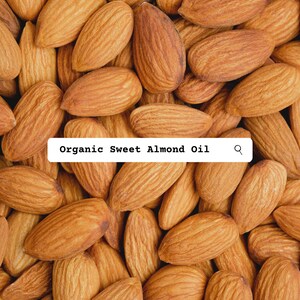 Pu&ograve; includere: Una collezione di mandorle grezze, marroni e di forma ovale con buccia ruvida disposte in un motivo denso. Un'etichetta rettangolare bianca &egrave; sovrapposta al centro, con il testo nero Organic Sweet Almond Oil e un'icona a forma di lente.