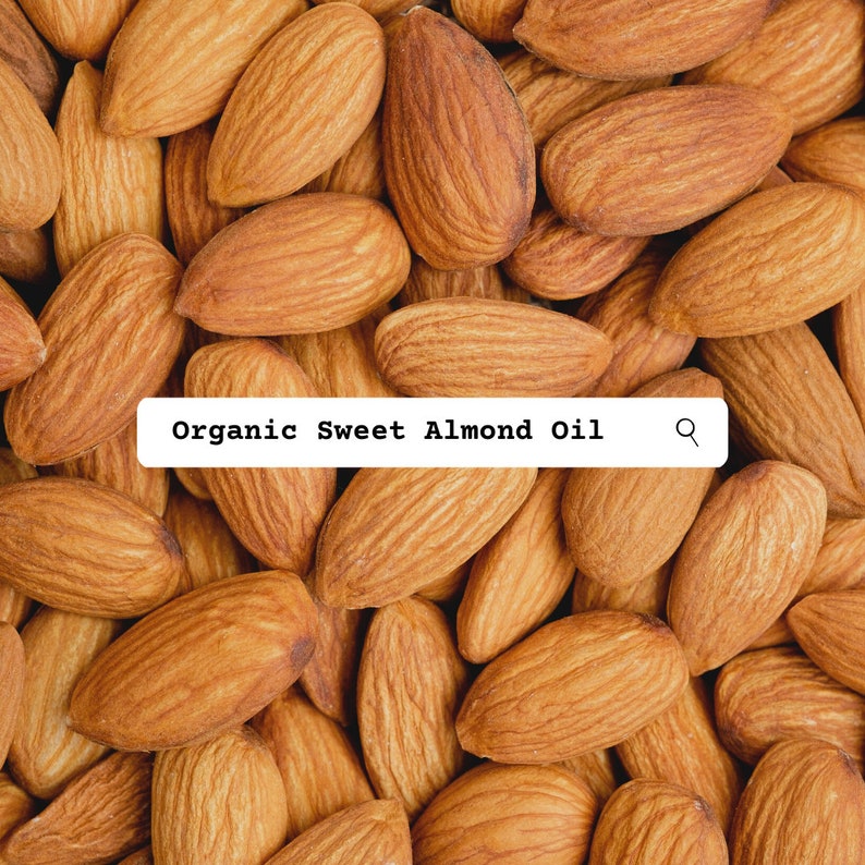 Pu&ograve; includere: Una collezione di mandorle grezze, marroni e di forma ovale con buccia ruvida disposte in un motivo denso. Un'etichetta rettangolare bianca &egrave; sovrapposta al centro, con il testo nero Organic Sweet Almond Oil e un'icona a forma di lente.