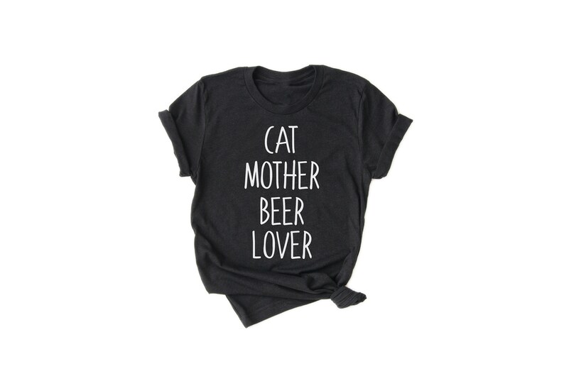 Może przedstawiać: Czarny T-shirt z białym napisem "Cat Mother Beer Lover".