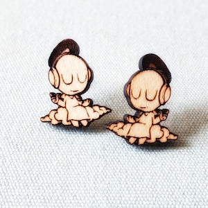 May include: Two wooden earrings featuring a cartoon character with headphones and a cloud design. The character is wearing a dress and has a simple face.