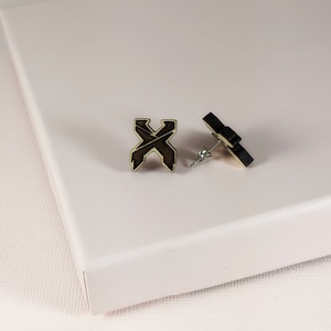May include: A pair of wooden earrings with a dark brown 'X' design. The earrings are on a white surface.