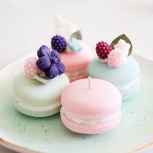 Peut inclure: Quatre bougies en forme de macarons de couleur pastel avec des décorations florales et de baies. Les bougies sont sur une assiette vert clair.