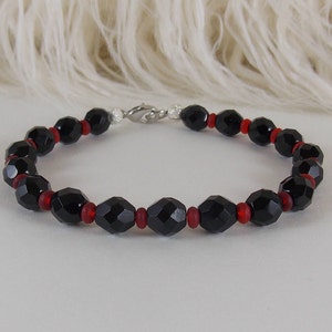 May include: A black and red beaded bracelet with a silver clasp. The bracelet is made with faceted black beads and smaller red beads.