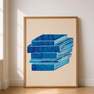 Könnte beinhalten: Ein gerahmter Kunstdruck mit einem Stapel blauer Aquarellbücher auf beigem Hintergrund. Die Bücher haben weiße Linien und einen Farbverlauf in Blautönen. Der Holzrahmen verleiht dem Kunstwerk eine natürliche Note.