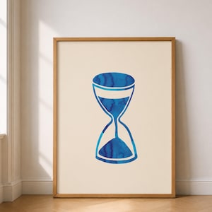 Könnte beinhalten: Gerahmter Druck mit einem blauen Sanduhr-Design. Die Sanduhr ist mit blauer Farbe im Aquarellstil gefüllt und vor einem cremefarbenen Hintergrund platziert. Der Rahmen besteht aus hellbraunem Holz und verleiht dem Kunstwerk eine natürliche Note.