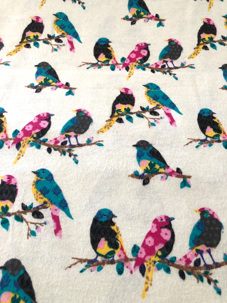 May include: A white fabric with a repeating pattern of colorful birds. The birds are black, blue, yellow, pink, and green. The birds are perched on branches with green leaves.