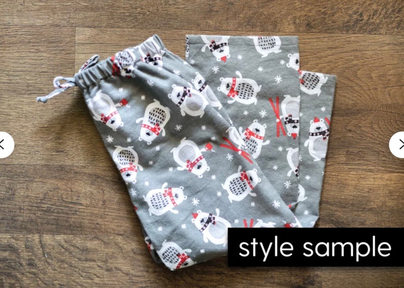 May include: Gray pajama pants with a repeating pattern of white polar bears wearing red scarves and hats. The bears are interspersed with red skis and white snowflakes. The pants have a drawstring waist and the words "style sample" in a black rectangle.
