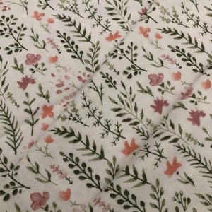 Puede incluir: Tela blanca con un estampado floral con hojas verdes y flores rosas y melocot&oacute;n. El dise&ntilde;o es un patr&oacute;n repetitivo de elementos bot&aacute;nicos, creando una est&eacute;tica suave y natural. La tela tiene una textura acolchada.