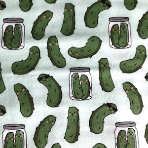 Puede incluir: Una tela verde claro con un patrón repetido de pepinillos de dibujos animados. Algunos pepinillos llevan gafas de sol y otros están en tarros de cristal. Los pepinillos tienen caras sonrientes y los tarros tienen un borde blanco y una tapa gris.