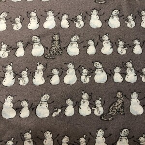 K&ouml;nnte beinhalten: Ein sich wiederholendes Muster auf grauem Hintergrund mit Schneem&auml;nnern mit ausgestreckten Armen, jeweils gepaart mit einem kleineren Schneemann. Dazwischen befinden sich Illustrationen von Katzen und Kaninchen. Die Schneem&auml;nner haben schwarze Arme und Karottennasen.
