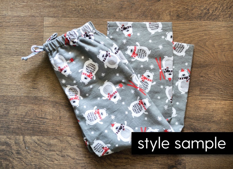 Puede incluir: Pantalones de pijama grises con un estampado repetido de osos polares blancos con bufandas y gorros rojos, con copos de nieve y gr&aacute;ficos de esqu&iacute; rojos. Los pantalones tienen cintura con cord&oacute;n y el texto "style sample".