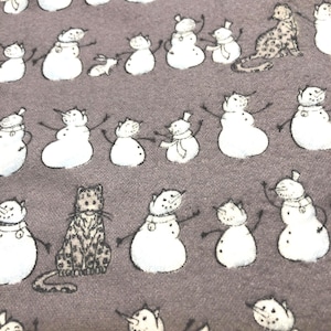 K&ouml;nnte beinhalten: Ein grauer Stoff mit einem sich wiederholenden Muster aus wei&szlig;en Schneem&auml;nnern mit schwarzen Stockarmen und Karottennasen. Dazwischen befinden sich Illustrationen von Katzen mit leopardenartigen Flecken. Die Schneem&auml;nner haben verschiedene Accessoires.