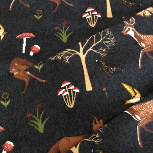 Pode incluir: Um tecido cinza escuro com um padr&atilde;o repetitivo de veados, cogumelos, &aacute;rvores e borboletas. O tecido tem uma textura macia e felpuda.