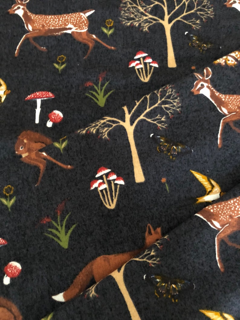 Pode incluir: Um tecido cinza escuro com um padr&atilde;o repetitivo de veados, cogumelos, &aacute;rvores e borboletas. O tecido tem uma textura macia e felpuda.