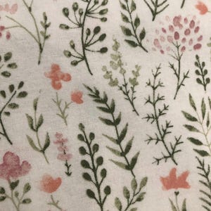 Puede incluir: Primer plano de una tela blanca con un estampado floral. El dise&ntilde;o presenta varias hojas y tallos verdes y oliva, junto con flores rosas y melocot&oacute;n. El patr&oacute;n est&aacute; distribuido uniformemente por la tela.