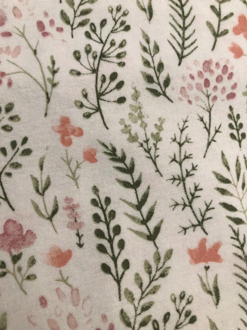 Puede incluir: Primer plano de una tela blanca con un estampado floral. El dise&ntilde;o presenta varias hojas y tallos verdes y oliva, junto con flores rosas y melocot&oacute;n. El patr&oacute;n est&aacute; distribuido uniformemente por la tela.